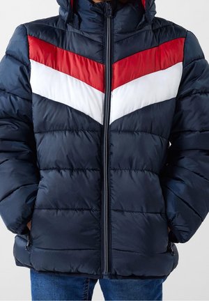 Doudoune marine avec des rayures en chevron rouges et blanches, fermeture éclair à l'avant et capuche. Surface texturée et matelassée avec poches zippées sur les côtés.