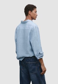 Light blue linen shirt with a relaxed fit, roll-up sleeves, and a button-down collar, paired with dark denim jeans.