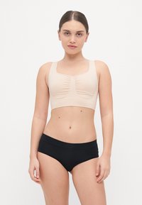Béžový crop top s designom zoskupeného stredu, širokými ramienkami a hladkou textúrou. Skombinovaný s čiernymi priliehavými šortkami, obe kusy sú priliehavé.