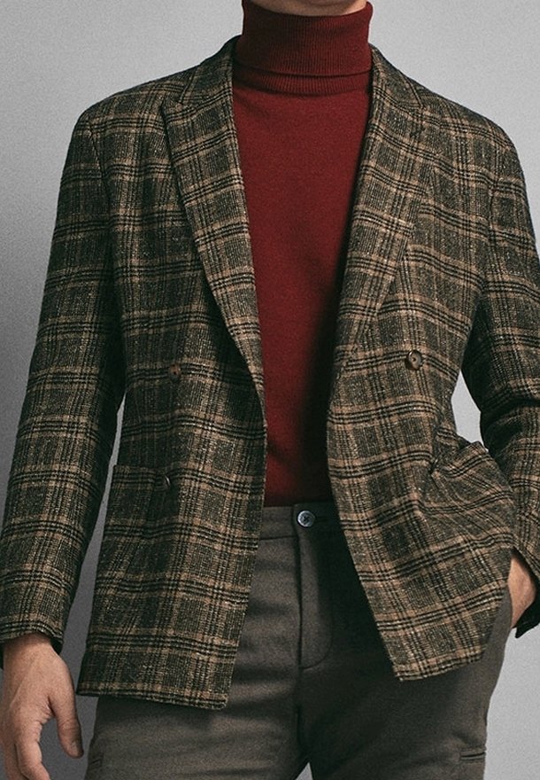 Blazer a scacchi marrone con chiusura doppiopetto e risvolto, indossato su un dolcevita color bordeaux; presenta un tessuto testurizzato e bottoni a vista.