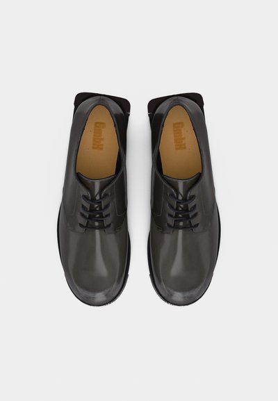 Ζευγάρι μαύρα δερμάτινα παπούτσια με κορδόνια, με θέα από πάνω, σε απλό ανοιχτό φόντο.