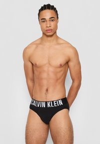 Zwarte katoenen slips met een witte "CALVIN KLEIN" logo op de tailleband. Glad textuur, slank ontwerp, en geen extra patronen of accenten.