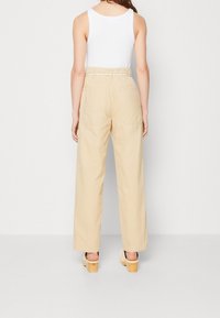 Beige kalhoty s širokými nohavicemi a vysokým pasem, které mají pletený pásek, dvě zadní kapsy a hladkou bavlněnou tkaninu.