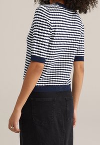 Marinblå och vit randig stickad topp med korta ärmar och ribbade mudd, som bärs med en svart kjol, vilket framhäver en avslappnad design.