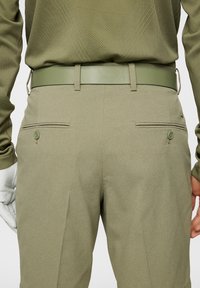 Vatsakirjaiset, vaaleanoliivinvihreät housut, joissa on rakennekuvioinen kangas. Housuissa on kaksi takataskua, joissa on napit, sekä yhteensopiva vyö.