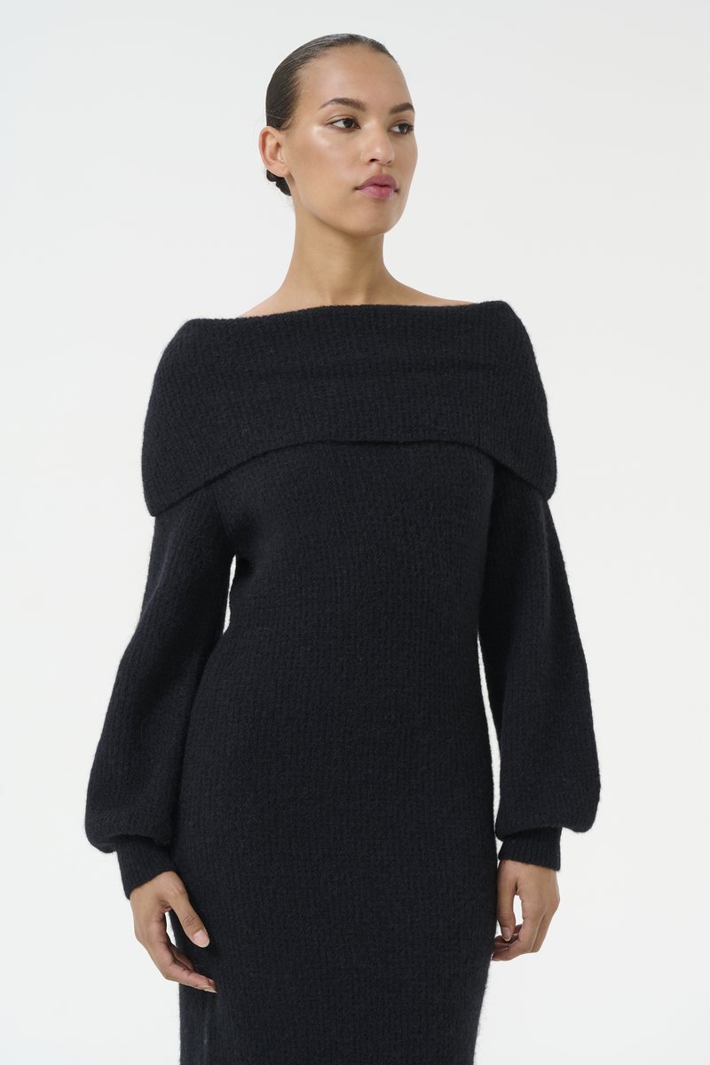 Abito maglione nero in maglia con design off-the-shoulder, maniche lunghe a palloncino, tessuto testurizzato e siluetta aderente.