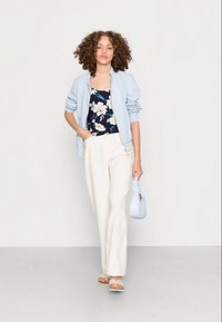 Casaco bomber azul claro, blusa floral azul-marinho, calças largas brancas e sandálias bege. Texturas suaves e uma mala azul claro.