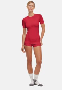 Maglietta crop rossa a maniche corte abbinata a pantaloni corti coordinati, realizzata in tessuto liscio e elastico. Presenta un marchio minimale sul petto.
