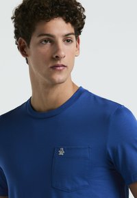 T-shirt en coton bleu avec un col rond, des manches courtes et une poche avec un petit logo de pingouin sur le côté gauche.