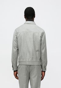 Γκρι μπλε ριγέ σακάκι με όρθιο γιακά, μανσέτες με κουμπιά και ελαστική μέση. Το ύφασμα έχει λεπτή υφή, δημιουργώντας μια ραμμένη εμφάνιση.