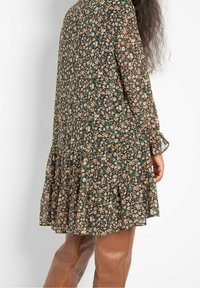 Blommig klänning med mörk bakgrund, små flerfärgade blommor, långa ärmar och volangkant. Mjuk, lätt tyg.