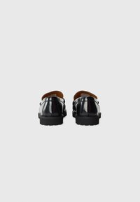 Zapatos negros de charol con forma redondeada, forro de cuero y suelas de goma texturizada, que presentan un hardware mínimo y un diseño elegante.