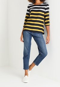 Gestreept top in zwart, wit en geel, met driekwartmouwen. Gecombineerd met lichtblauwe, rechte jeans en witte instappers.