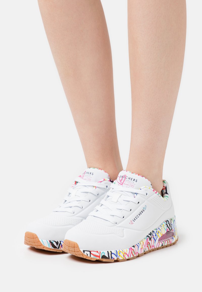 Weiße Sportschuhe mit bunten, gemusterten Akzenten an der Sohle. Obermaterial aus Mesh, runde Zehenpartie und abgerundete Ferse. Mit Schnürsenkeln und gepolstertem Kragen.