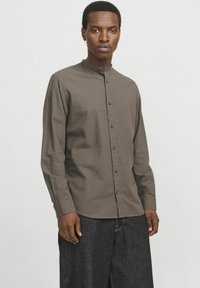 Brown button-up shirt with a stand collar and long sleeves, featuring a textured fabric and contrasting metallic buttons.