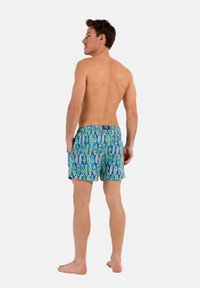 Shorts de bain pour hommes en bleu avec un motif de feuilles vibrant en vert, orange et blanc. Dotés d'une taille élastique et de poches latérales.