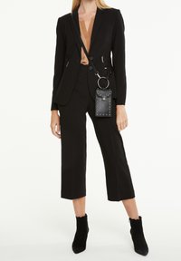 Černý ušitý oblek s krátkými kalhotami, v kombinaci se světlým béžovým topem. Obsahuje černou přes rameno tašku se cvočky a kulatým kovovým akcentem.