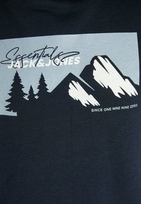 T-shirt en coton bleu marine avec un graphique de montagne en bleu clair, intégrant des éléments forestiers et le texte "Essentials JACK & JONES" au-dessus.