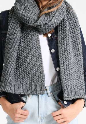 Écharpe grise épaisse en tricot enroulée autour du cou, portée sur une chemise blanche et une veste en denim foncé, associée à un jean bleu clair.