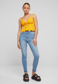 Žlutý pruhovaný crop top s vázáním ve středu a volánkovým lemem, v kombinaci s světle modrými skinny džíny s vysokým pasem a černými platformovými sandály.