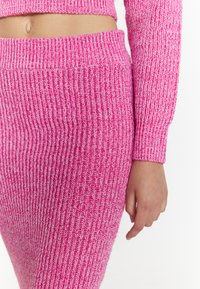 Geribbelde gebreide trui en rok set in felroze met contrasterende witte draad. Heeft een aansluitend ontwerp met lange mouwen en een hoge taille.