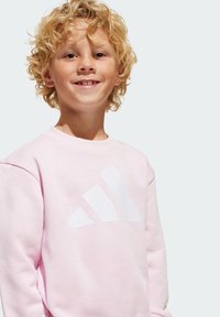 Sweatshirt rose clair avec un col rond, arborant un grand logo Adidas blanc. Fabriqué en tissu doux avec une texture lisse.