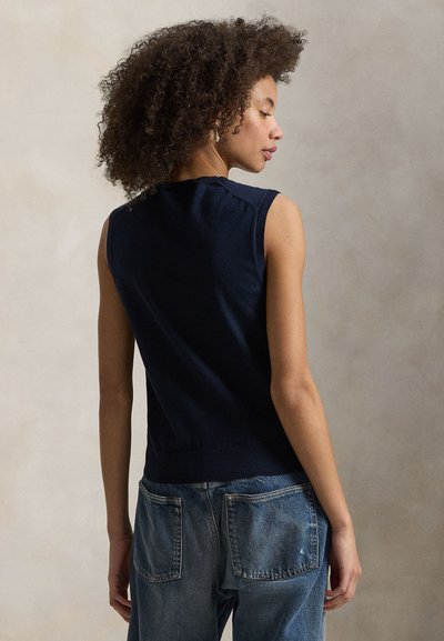 Σκούρο μπλε, μαν sleeveless πουλόβερ με ριγωτή υφή, εφαρμοστό στη μέση. Συνδυάζεται με τζιν παντελόνι μέσης μεσαίου ύψους με πίσω τσέπες.