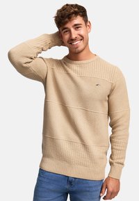Pull en tricot beige avec des motifs texturés et des poignets et ourlet côtelés. Présente un logo bleu sur la poitrine et un col rond.