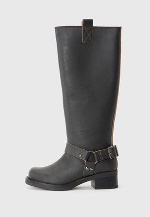 Black leather knee-high boot with a textured finish, featuring a side buckle accent and a low heel. Detailed stitching along the seams.