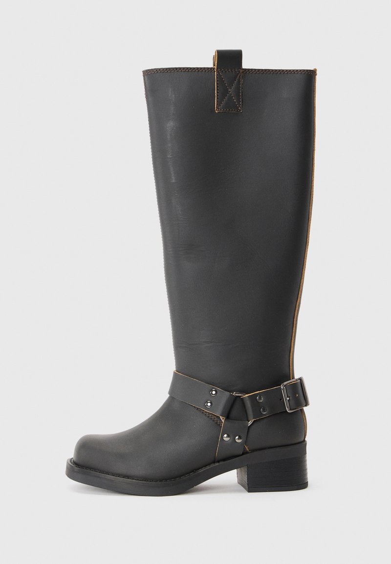 Bota de cuero negro hasta la rodilla con un acabado texturizado, que presenta un acento de hebilla lateral y un tacón bajo. Costura detallada a lo largo de las costuras.