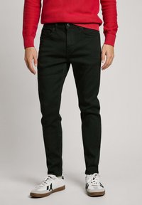 Black denim jeans with a slim fit and a smooth texture, paired with white sneakers featuring black accents and a light brown sole.
