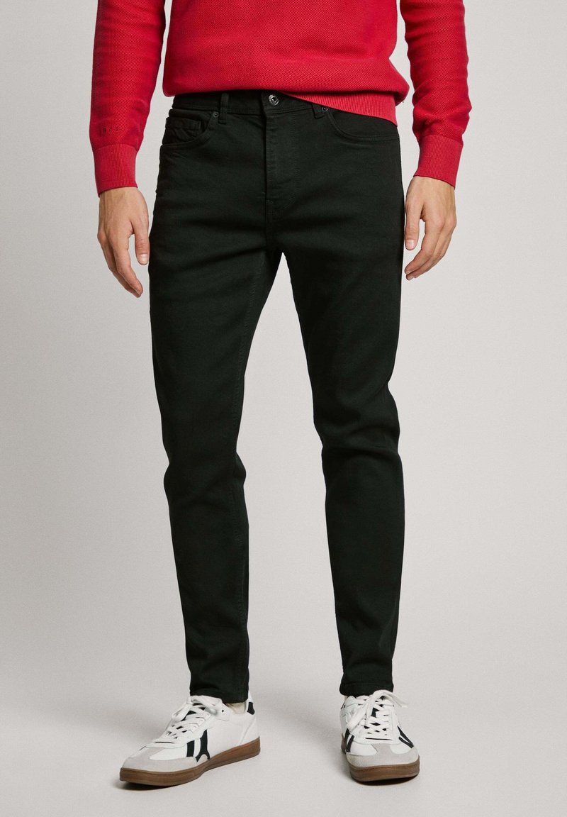 Black denim jeans with a slim fit and a smooth texture, paired with white sneakers featuring black accents and a light brown sole.