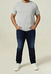 Grå t-shirt med kort ärm, mörkblå jeans, vita skor. Åtsittande design med mjukt tyg; avslappnad stil utan synliga logotyper eller mönster.