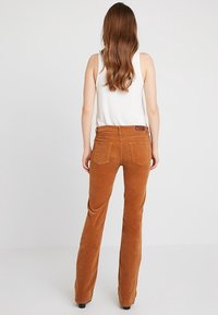 Bruine corduroy flared broeken met een zachte, textuurafwerking. Beschikt over twee achterzakken en een label op de tailleband.