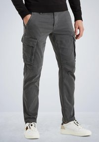 Graue Cargo-Hosen aus Twill-Gewebe mit seitlichen Taschen, einer schmalen Passform und einem Reißverschluss. Kombiniert mit weißen Sportschuhen.