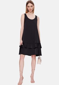 Vestido negro sin mangas con escote redondo y dobladillo con volantes en capas. Confeccionado en una tela suave, tiene un corte holgado y un diseño de largura media.