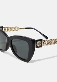 Ochelari de soare tip cat-eye cu rame din acetat negru, lentile gri închis și accesorii din lanț auriu pe brațe, având un detaliu cu logo.