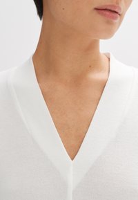 Witte V-hals gebreide trui met een subtiele textuur, vervaardigd van een gladde, zachte stof met strakke lijnen, omringd door een licht geribde kraag.