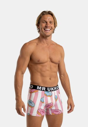 Man zonder shirt die lacht, draagt roze-wit gestreepte boxershorts met blauw-roze donutpatroon en een zwarte tailleband met het opschrift "MR UKKO".