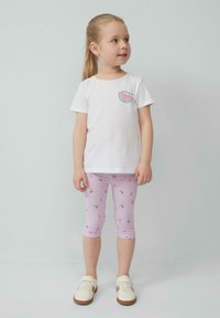 Biały t-shirt z krótkim rękawem z grafiką arbuza, w połączeniu z różowymi legginsami capri z kwiatowym wzorem, uzupełniony białymi sneakersami.
