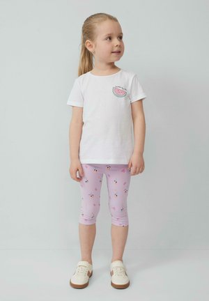 Biały t-shirt z krótkim rękawem z grafiką arbuza, w połączeniu z różowymi legginsami capri z kwiatowym wzorem, uzupełniony białymi sneakersami.
