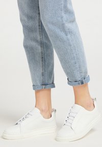 Sneakers din piele albă cu un design elegant, având un panou pentru șireturi ascuns și o talpă din cauciuc texturată, asortate cu blugi deschiși la culoare, rulați.