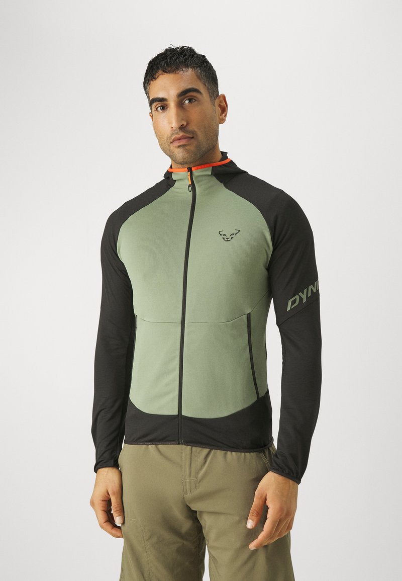 Green and black jacket with long sleeves, zipper, and logo on sleeve. Features contrasting colors and a fitted design, made from breathable material.