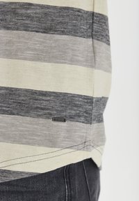 Camiseta de rayas con rayas horizontales en color crema, gris y azul marino. La tela es liviana y tiene una pequeña etiqueta de logo negra en la costura lateral.