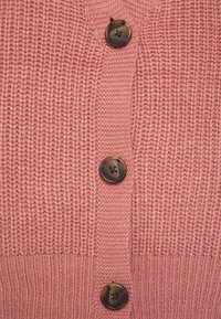 Stickad rosa cardigan med ribbat mönster och fem bruna knappar fram, som framhäver en klassisk design och mjukt material.