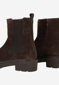 Brown suede ankle boots with elastic side panels, back pull tab, and a side zipper. Chunky sole with stitching detail.