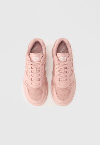 Ζευγάρι ανοιχτό ροζ αθλητικά παπούτσια Coach με κορδόνια, λογότυπο στην γλώσσα και σχέδιο πλέγματος στην περιοχή των δακτύλων, τοποθετημένα σε απλή λευκή επιφάνεια.