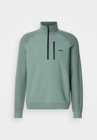 Hellgrüner Pullover mit hohem Kragen, halbem Reißverschluss, gerippten Bündchen und einem kleinen schwarzen Logo auf der Brust. Aus glattem Material mit strukturierten Akzenten.