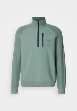Suéter de color verde claro con un alto cuello, media cremallera, puños acanalados y un pequeño logo negro en el pecho. Presenta un material suave y detalles texturizados.