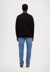 Juodas džemperis ilgomis rankovėmis, su apvalia iškirpte ir rebuotais rankogaliais, derinamas su šviesiai mėlynomis džinsomis ir tamsiais sportbačiais. Atsukta nugaros pusė.